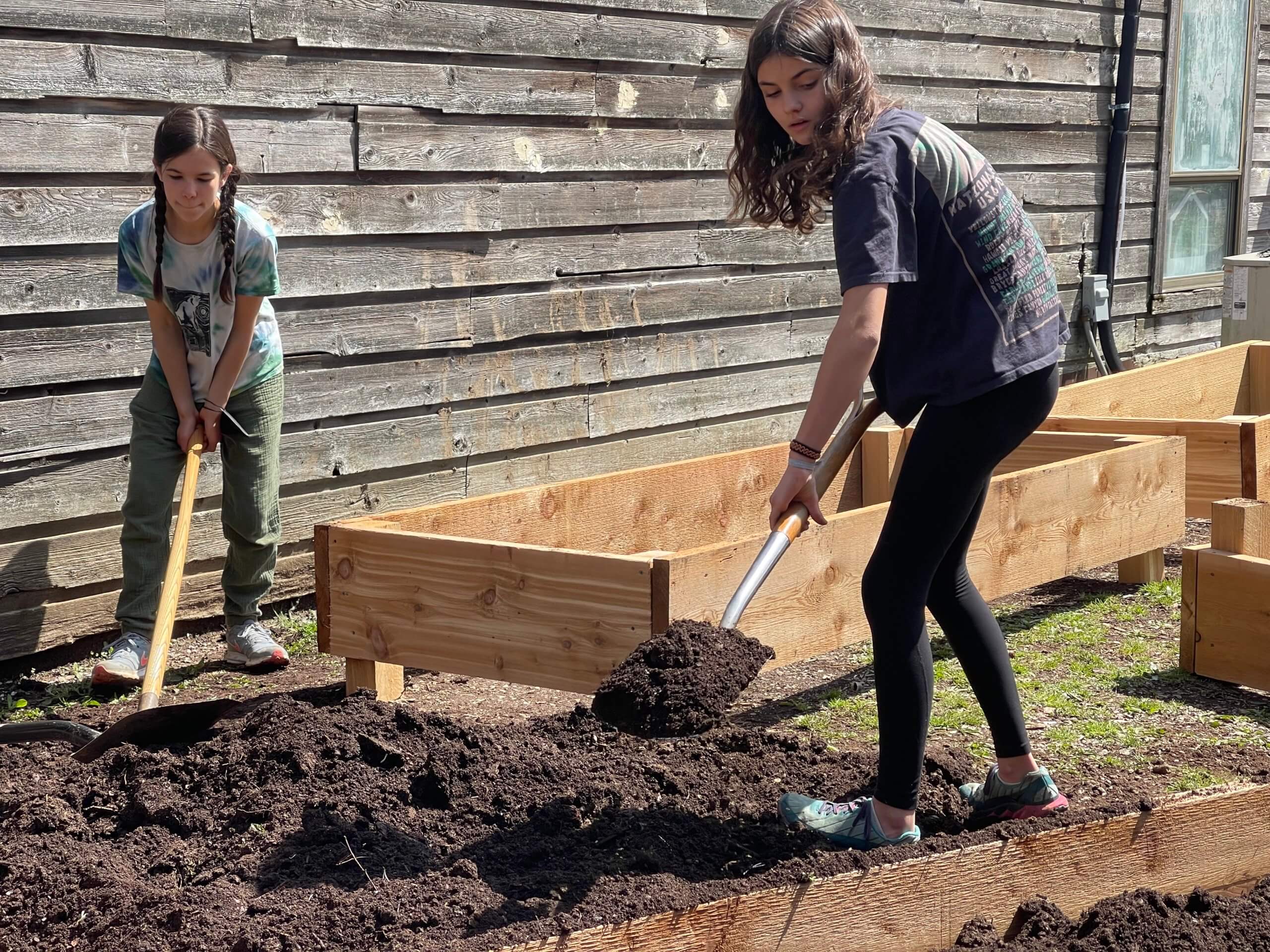 two girls shoveling dirt into garden beds
